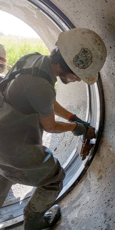Field Technician expanding the retaining bands, locking the EPDM rubber in place over a pipe joint