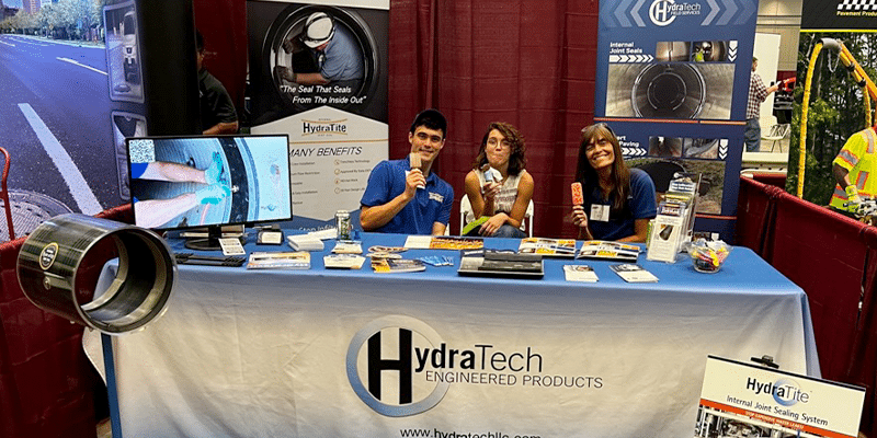 Three people sitting at HydraTech's booth at APWA