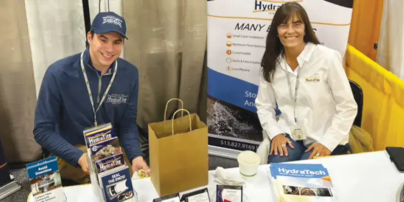 Two HydraTech representatives sitting behind a table in their booth at OTEC