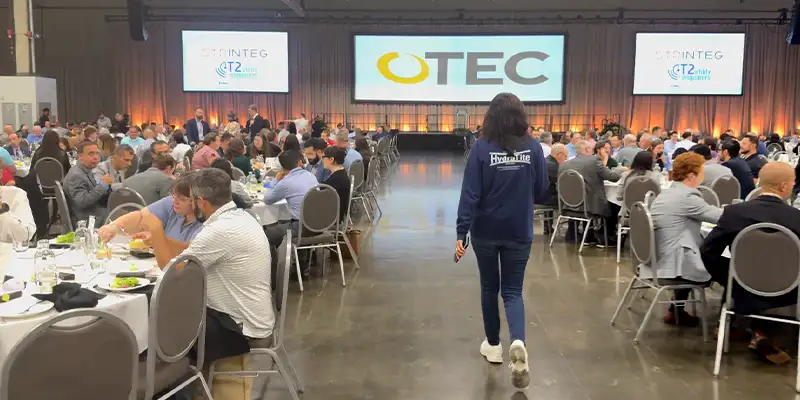 a woman walking through a room full of people eating lunch